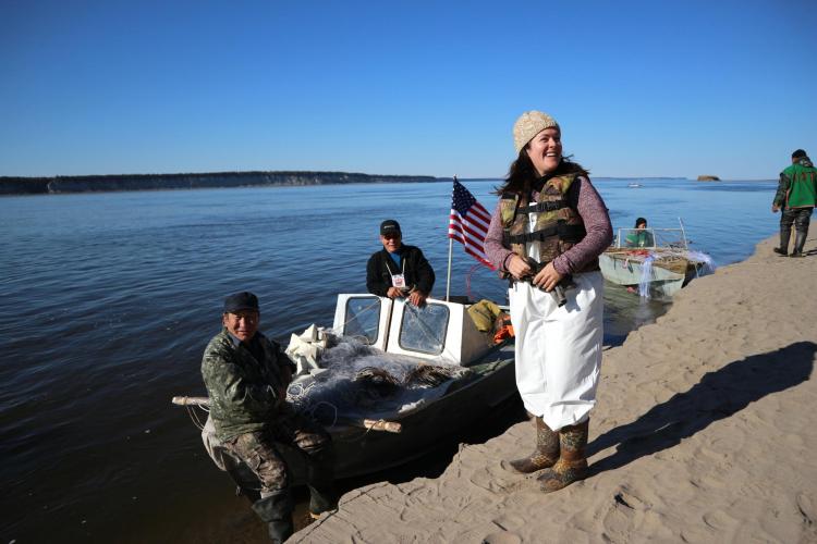 Skiff boat on a river parked along a shore with woman standing on sand