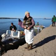 Skiff boat on a river parked along a shore with woman standing on sand