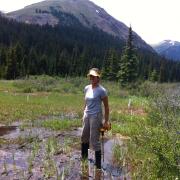 Woman standing in mountain puddle with drill and mountain backdrop 