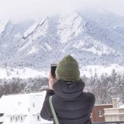 Student taking a picture of the snowy Flatirons