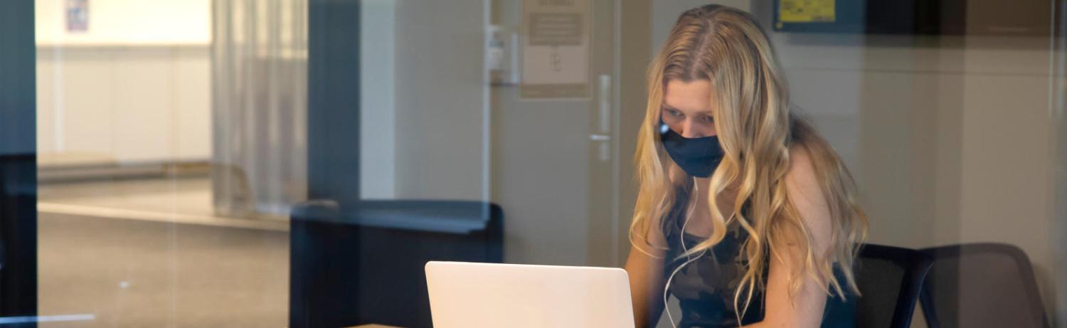 Grad student with long hair in a mask looking intently at her laptop. 