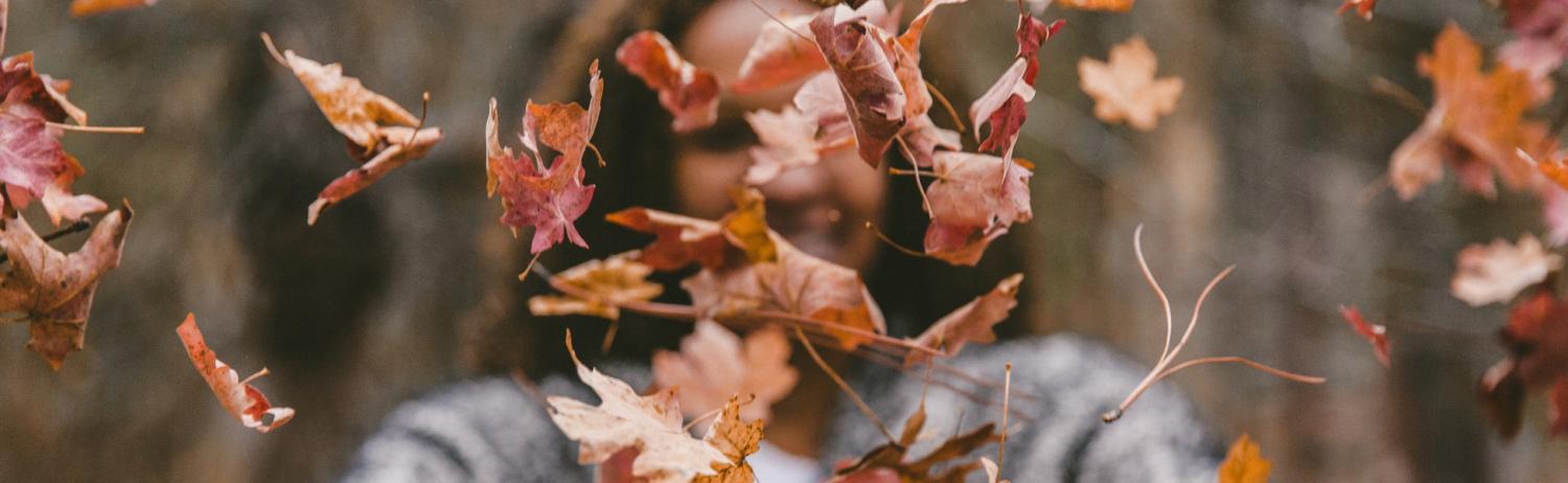 Girl throwing colorful fall leaves in the air in front of her face. 