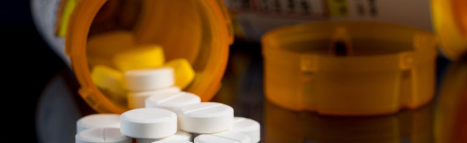 Photo of a prescription pill bottle laying open with pills coming out on a table.
