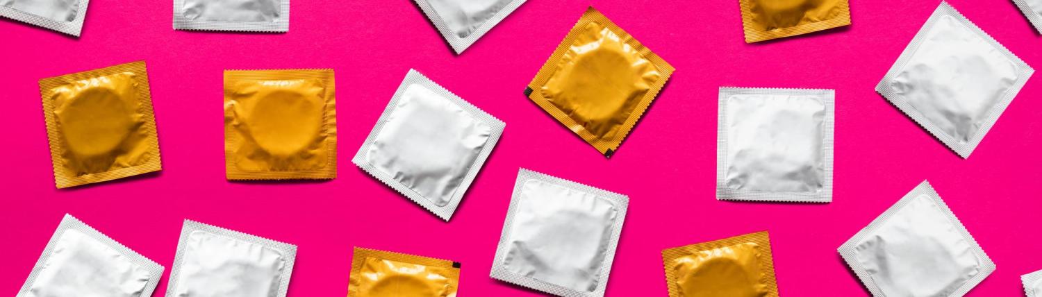 Photo of different colored condom packages on a hot pink background.