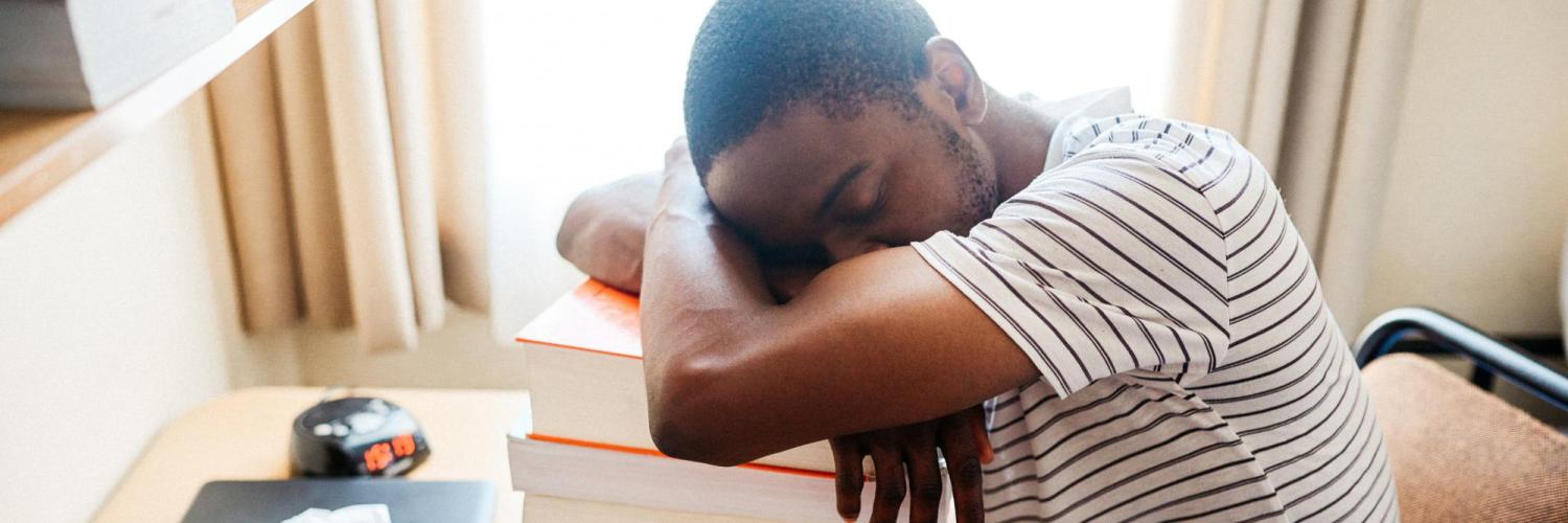 Student sleeping at his desk on a pile of textbooks.