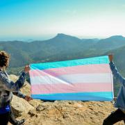 Photo of two people holding up a transgender pride flag.