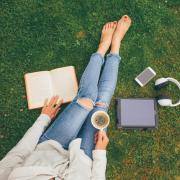 Person laying in the grass with headphones, a laptop and coffee