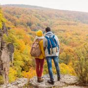 Two students bundled in sweaters standing on a hilltop overlooking colorful fall foliage.