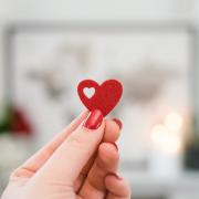 Photo of a hand with red nails holding up a heart cutout.