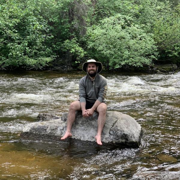 Kevin Harris sits on a rock in a river.