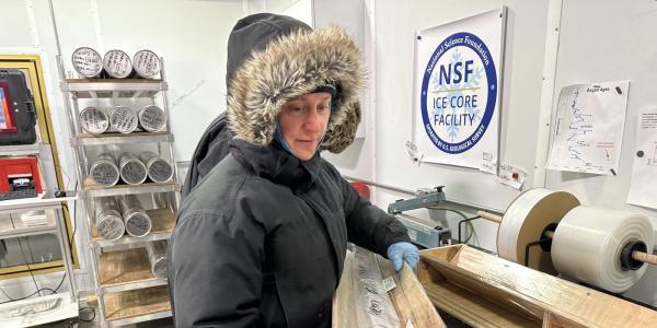 Valerie Morris, in puffy fur-lined parka, carries a section of the GISP2 ice core in a wooden tray at the NSF Ice Core Facility.