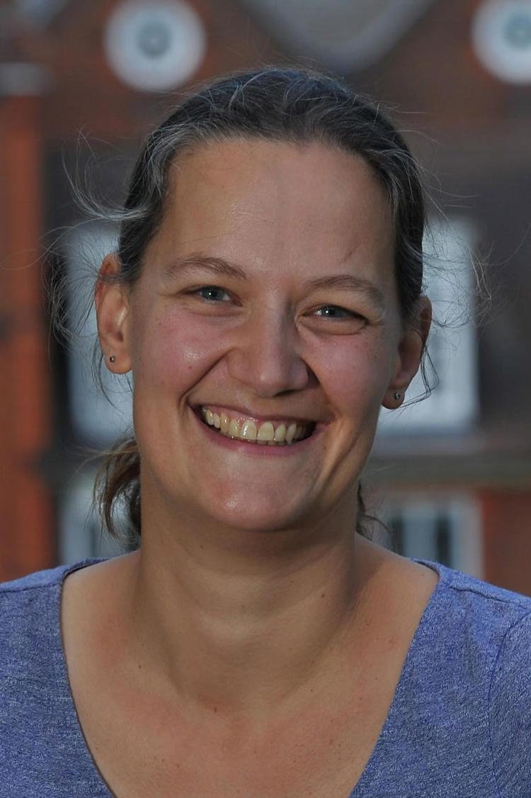 A woman in a pastel blue scoop neck shirt smiles for a portrait