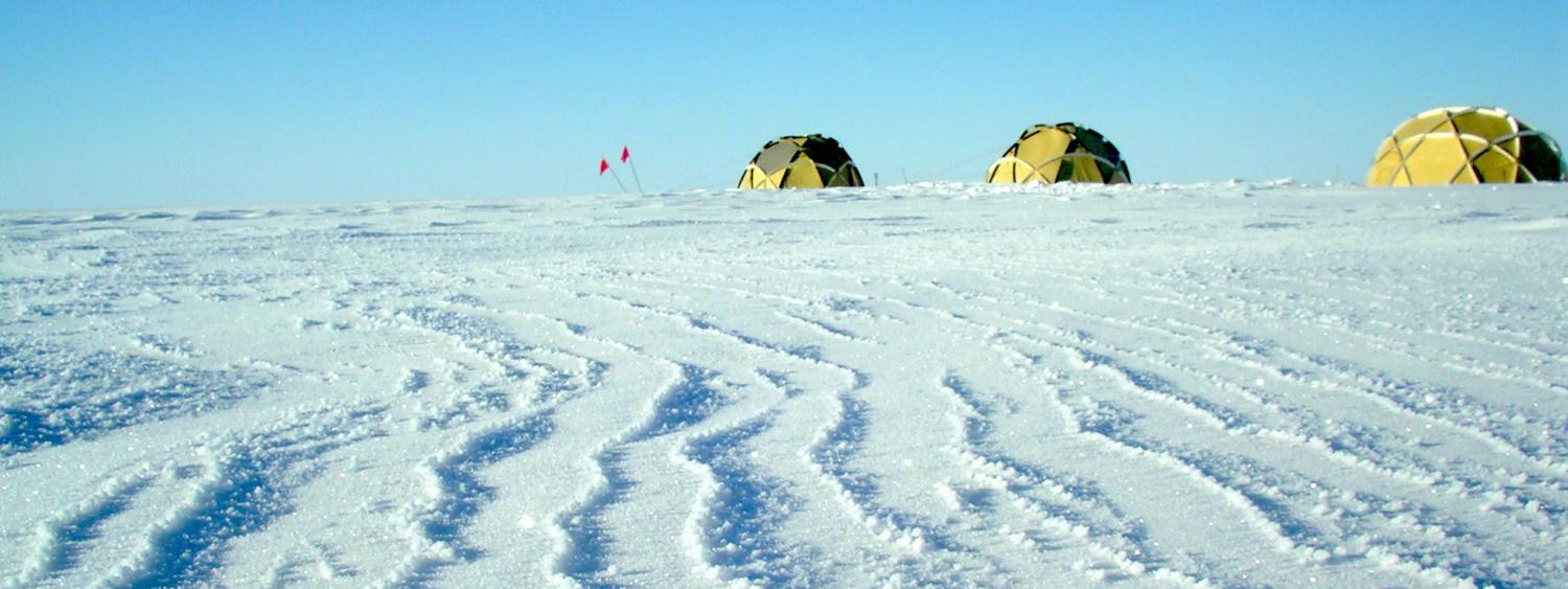 Sparkly ridged snow drifts on the Greenland Ice Sheet with yellow dome tents site on the horizon 