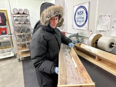 Valerie Morris, in puffy fur-lined parka, carries a section of the GISP2 ice core in a wooden tray at the NSF Ice Core Facility.