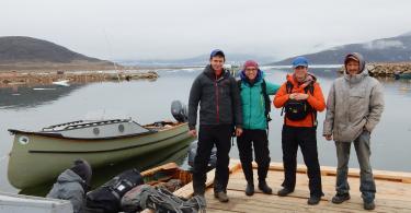 Nicolas Young, Sarah Crump, Simon Pendleton, and Gordie Audlakiak stand on a dock preparing to depart icy and cloudy Qikiqtarjuaq, Nunavut