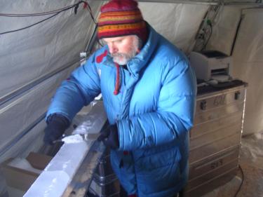 Bruce sampling an ice core in a cold tent wearing a big blue puffy jacket
