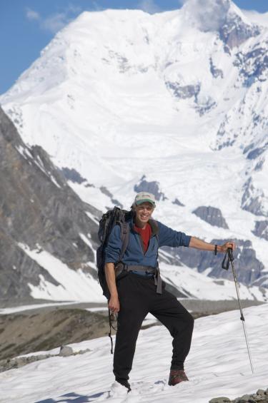 Bob Anderson takes a break on an Alaskan snowfield with glaciated mountain behind him.