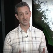 Noah Molotch speaks in front of a large satellite image of snow cover in California.