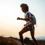 Peyton, a young Black woman wearing a t-shirt, shorts, and backpack, runs along the ridgeline of a mountain trail.