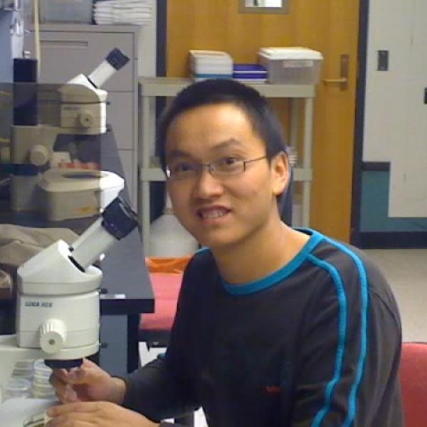Qinghua Zhou Posing Next to a Microscope 
