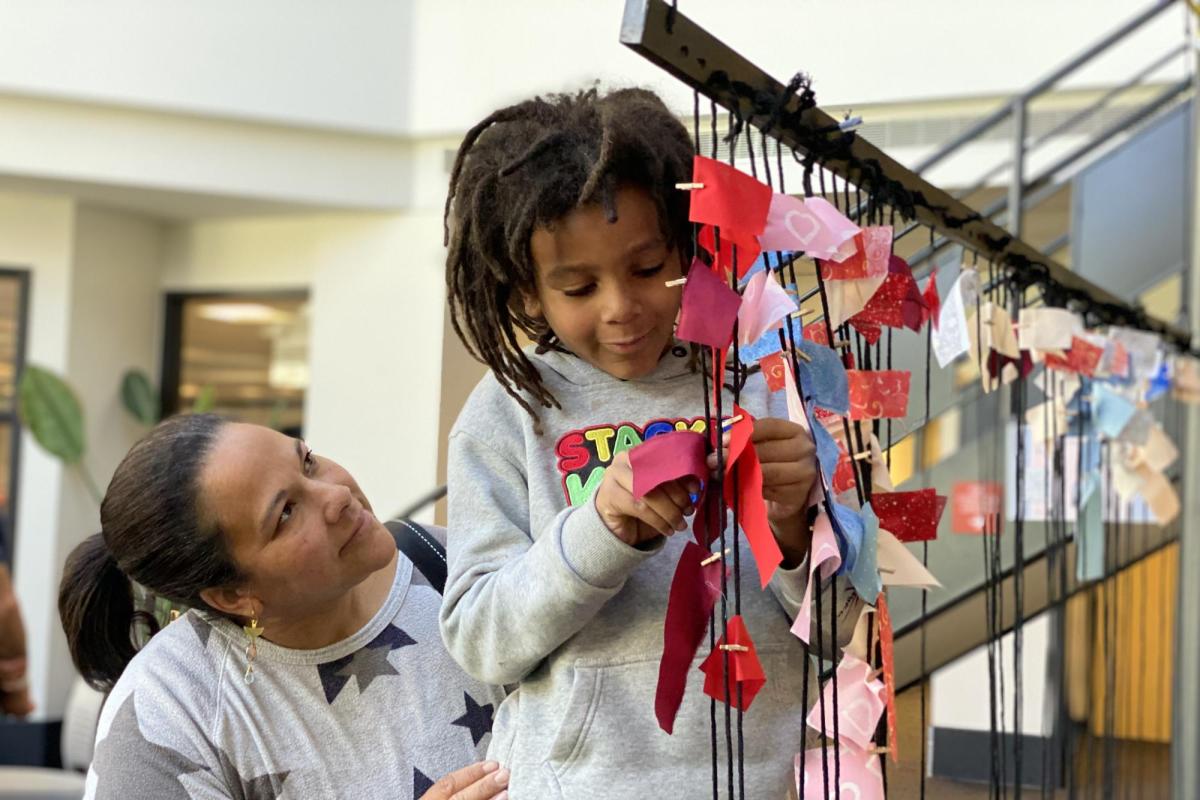 A woman looks up at her child who is attaching a piece of paper to a large mobile