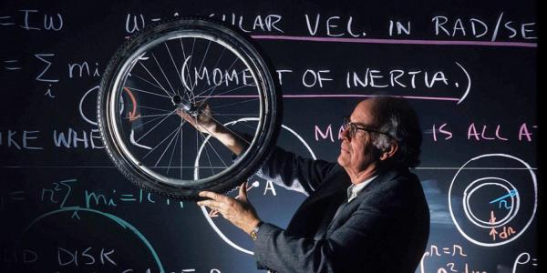 person with a bicycle wheel in front of a chalkboard