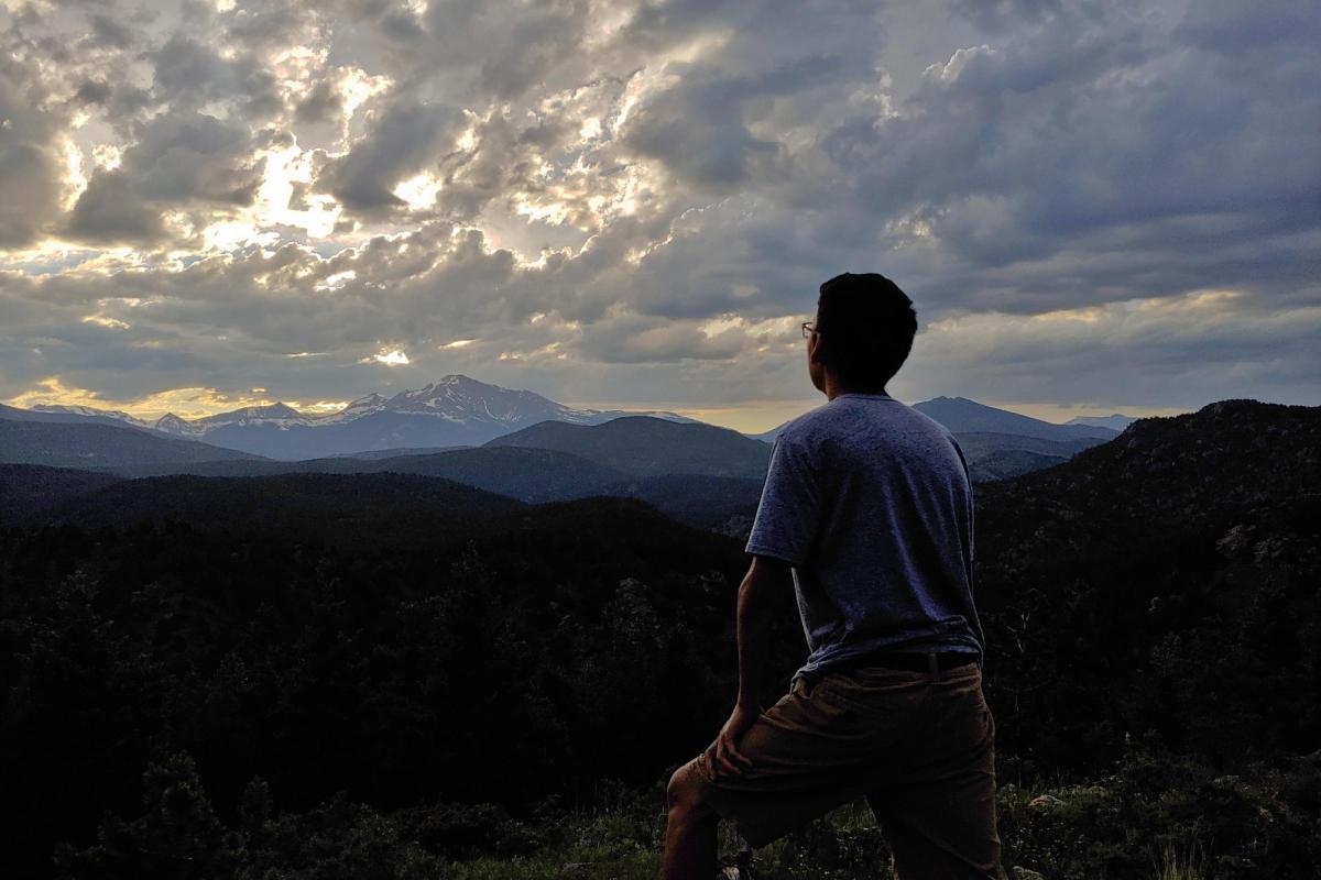 a student standing on a cliff facing out towards the sunset