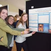 four students gesture at a research poster with the title Basketball or Swimming