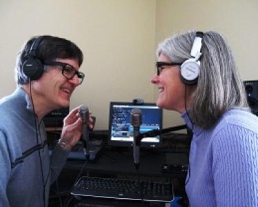 Peter and Nancy Torpey wearing headphones and posing by their podcast recording equipment.
