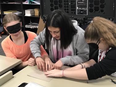 Girls with blindfolds play tactile Pictionary game.