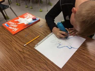 Boy creates a tactile picture for a storybook using a 3D pen.
