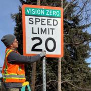 Worker installs a Vision Zero speed limit sign.