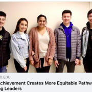 Five students stand against hallway wall smiling.