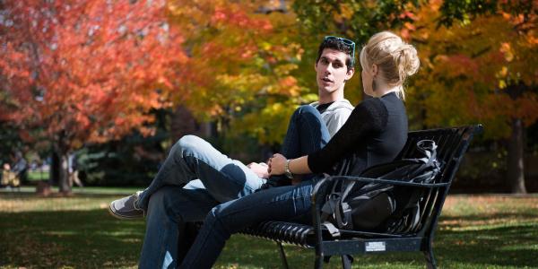 Two people having a conversation on a bench outdoors