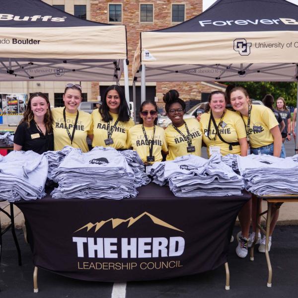 Volunteers from The Herd pose with their booth giving out free CU swag