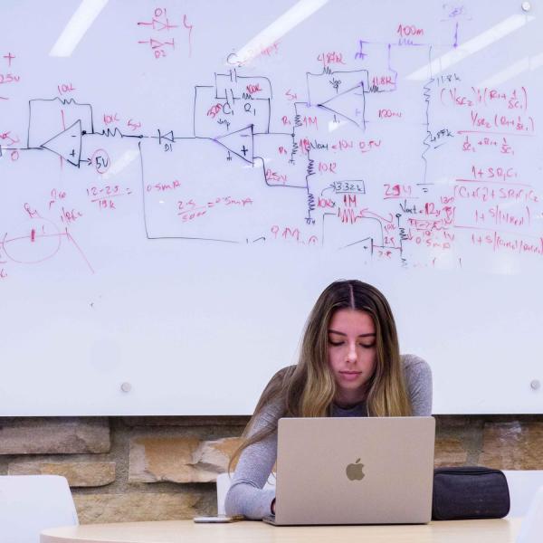 A student works out a homework question on a whiteboard