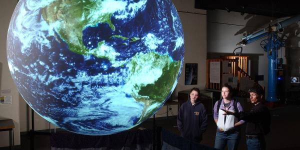 Students looking at lighted globe or Earth