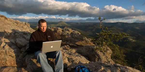 Professor on laptop in the mountains