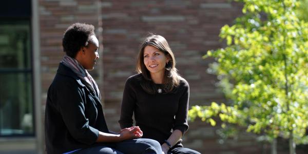 Two people having a conversation on a bench outside