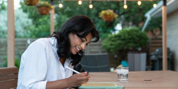 Student sitting at a table writing on a tablet