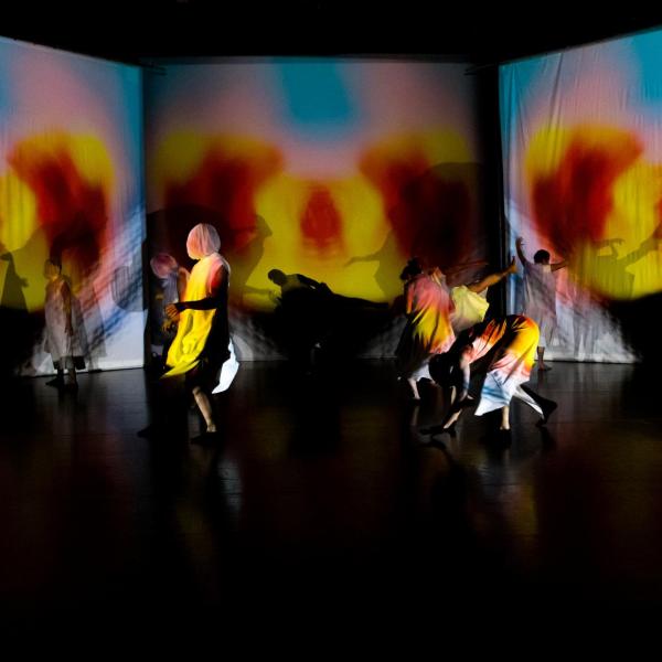 Students performing in multi-colored costumes and light