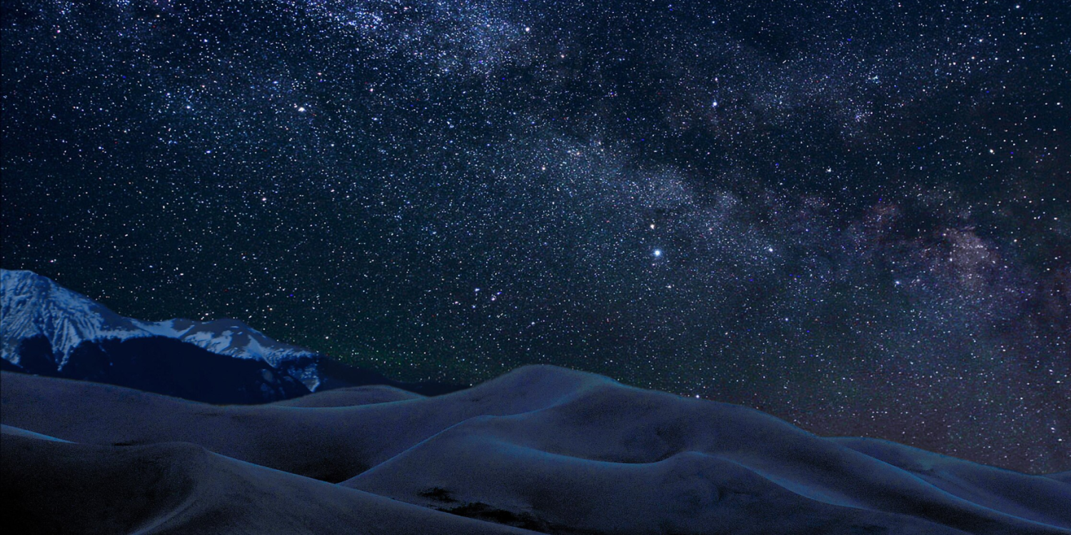 Stars in the night sky above sand dunes