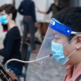 Student plays a musical instrument with a mask and a face shield on.