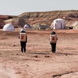 Two people wearing spacesuits walk through the Utah desert