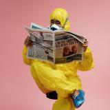 A stock image of a man in a hazardous materials suit reading a newspaper.