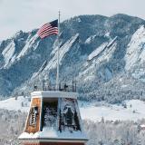 A snow-dusted Old Main tower with the Flatirons in the background.