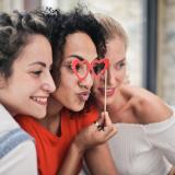 Three friends posing for a photo, one with red heart-shaped glasses