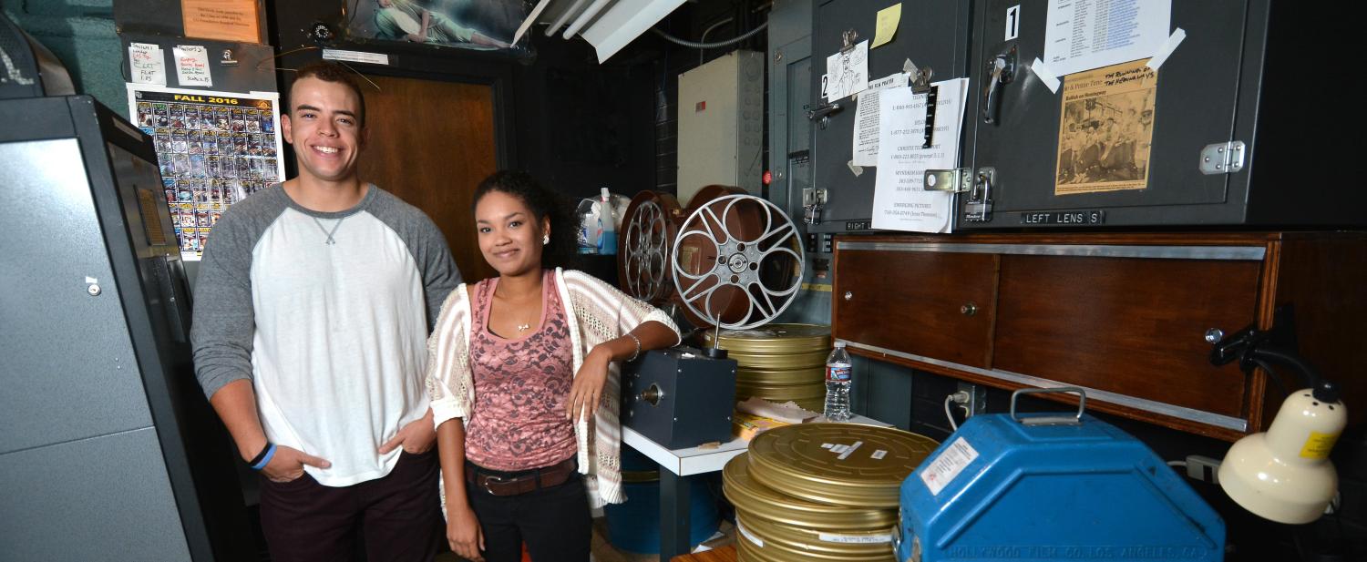 Adam Elbeck and Melina Dabney pose in the CU Boulder film lab with stacks of movie reels