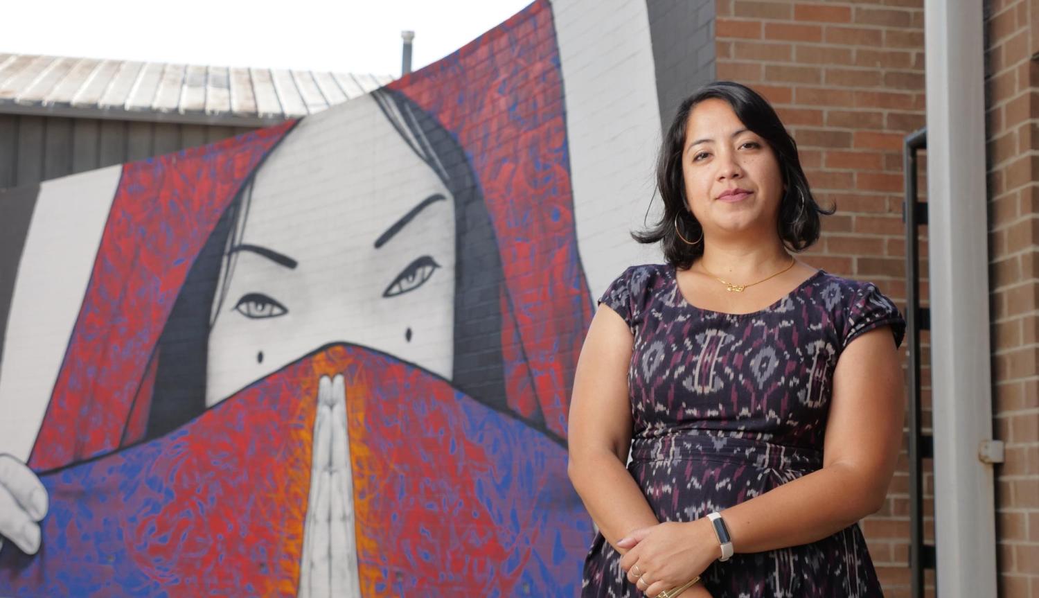 Noreen Naseem Rodriguez stands in front of a mural depicting a woman holding fabric over her face