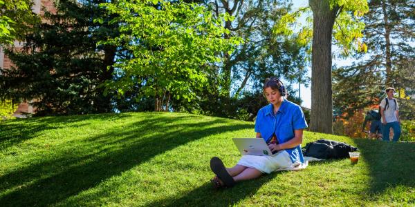 student working on laptop outside on campus